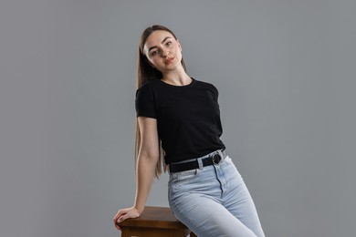 Photo of Beautiful young woman in stylish jeans sitting on stool against grey background