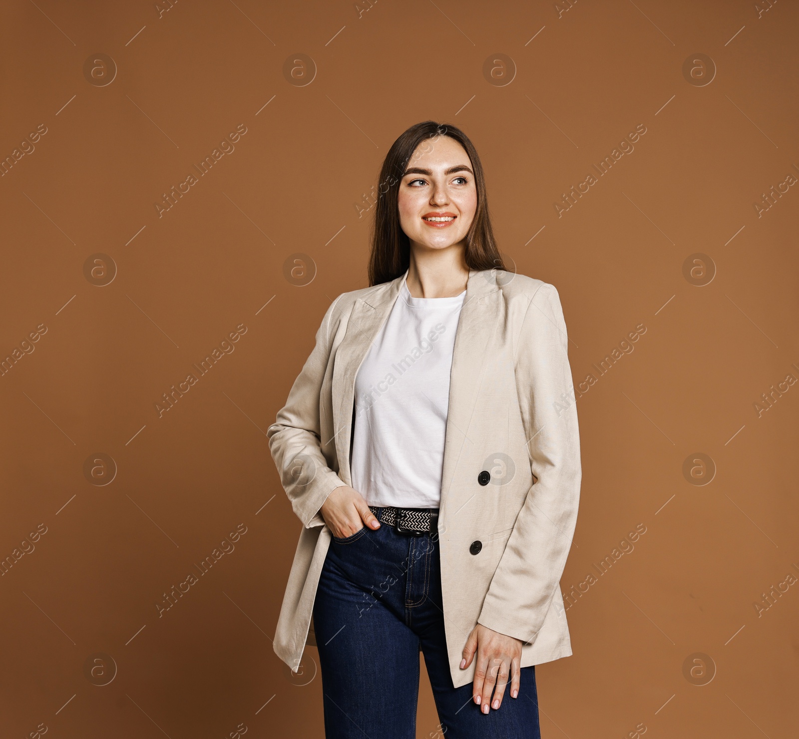 Photo of Smiling woman in stylish jeans on brown background. Space for text