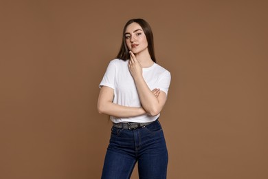 Beautiful young woman in stylish jeans on brown background