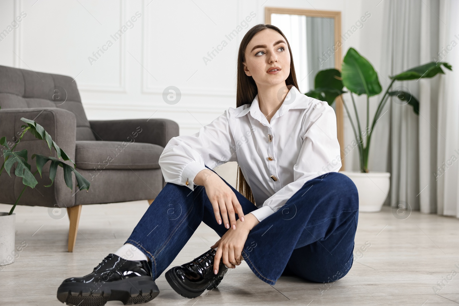 Photo of Beautiful young woman in stylish jeans sitting on floor at home