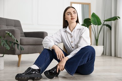 Photo of Beautiful young woman in stylish jeans sitting on floor at home