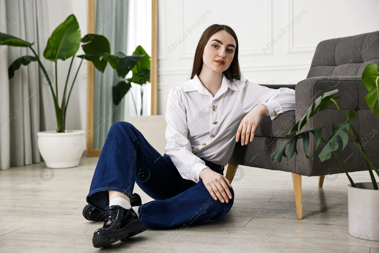 Photo of Beautiful young woman in stylish jeans sitting on floor at home