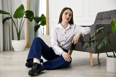 Beautiful young woman in stylish jeans sitting on floor at home