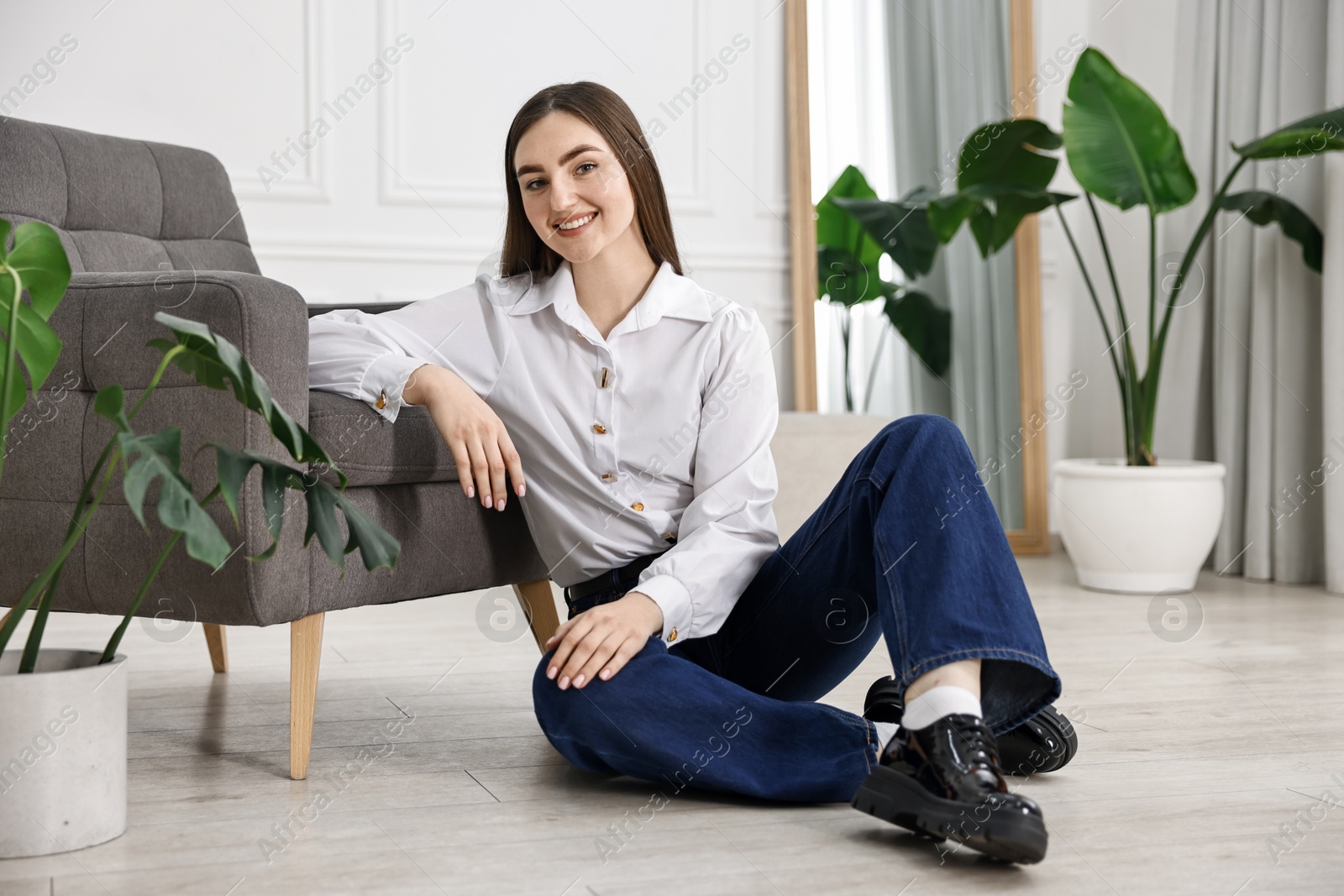 Photo of Smiling woman in stylish jeans sitting on floor at home