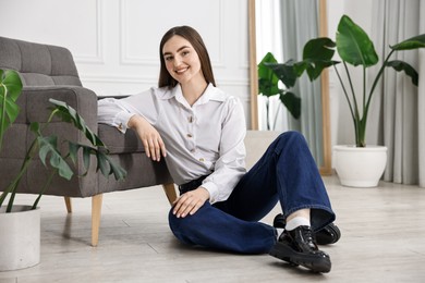 Smiling woman in stylish jeans sitting on floor at home