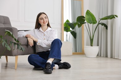 Photo of Smiling woman in stylish jeans sitting on floor at home. Space for text