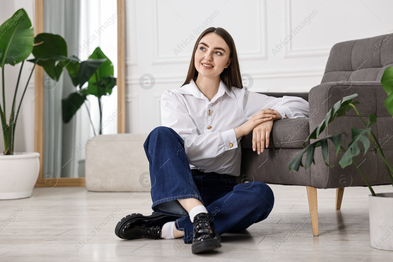 Photo of Smiling woman in stylish jeans sitting on floor at home