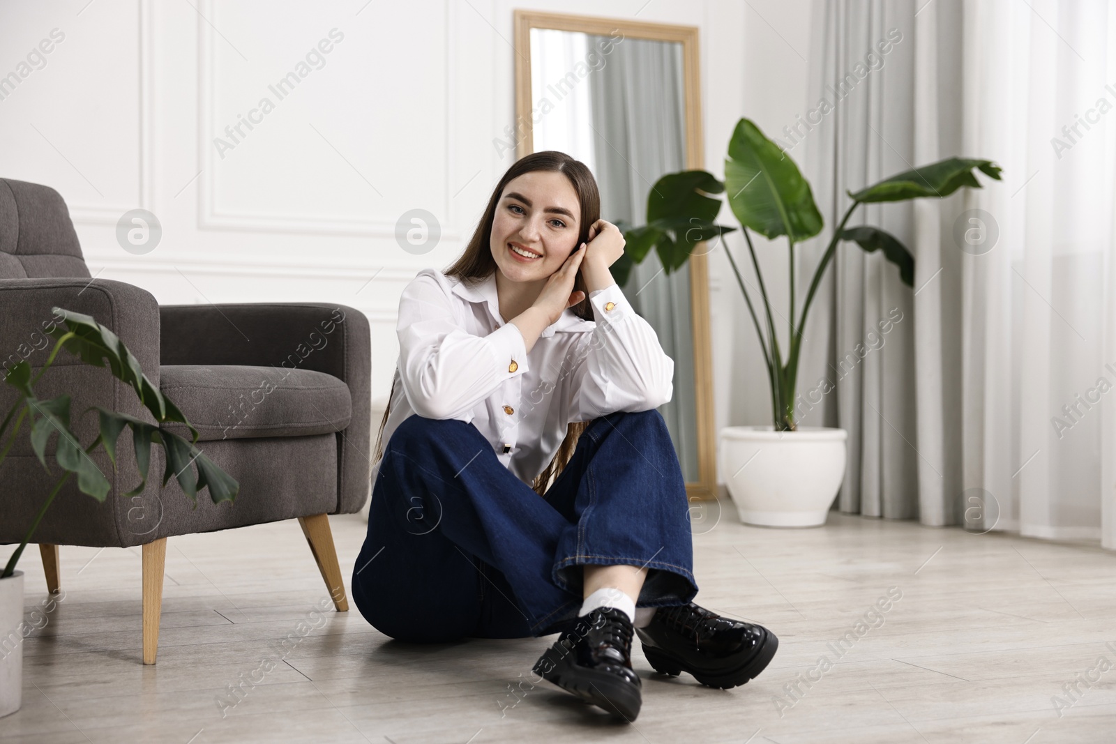 Photo of Smiling woman in stylish jeans sitting on floor at home