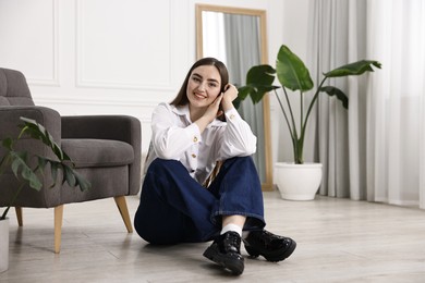 Smiling woman in stylish jeans sitting on floor at home