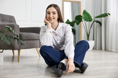 Smiling woman in stylish jeans sitting on floor at home