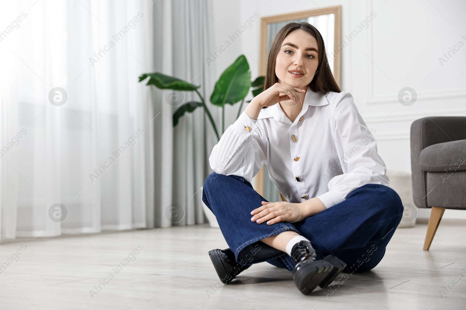 Photo of Woman in stylish jeans sitting on floor at home. Space for text