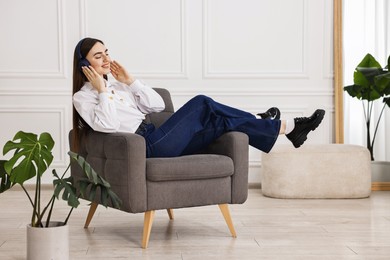 Smiling woman in stylish jeans listening to music on armchair at home