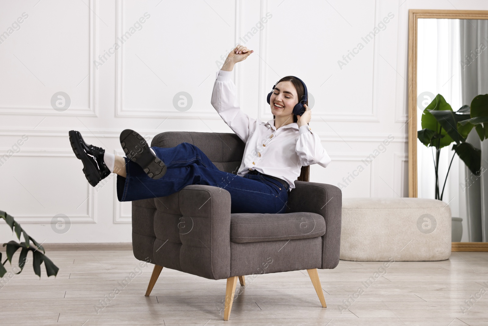 Photo of Smiling woman in stylish jeans listening to music on armchair at home