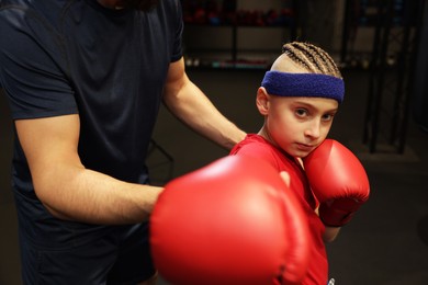 Photo of Boy in protective gloves with his boxing coach at training center