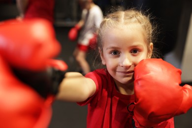 Photo of Girl in protective gloves having boxing practice indoors