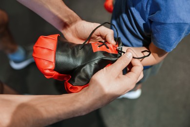 Photo of Boxing. Coach helping girl to put on protective gloves before training indoors, closeup