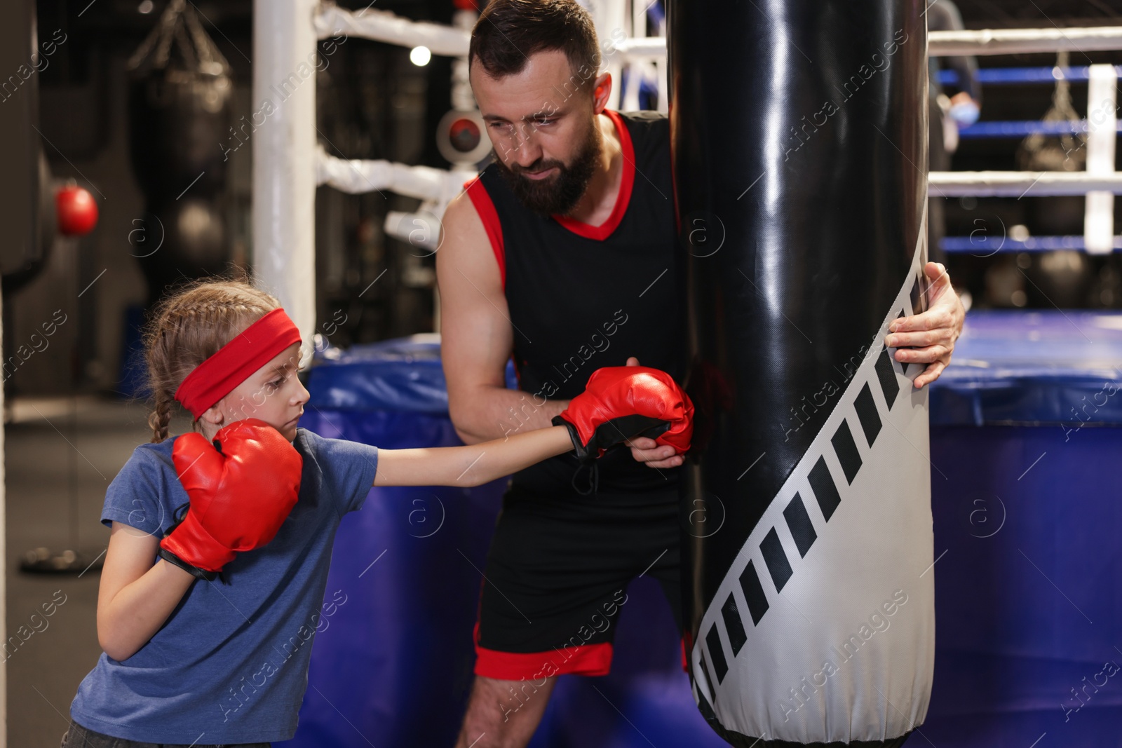 Photo of Girl in protective gloves having boxing practice with her coach at training center