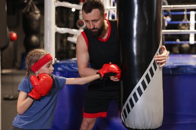 Photo of Girl in protective gloves having boxing practice with her coach at training center