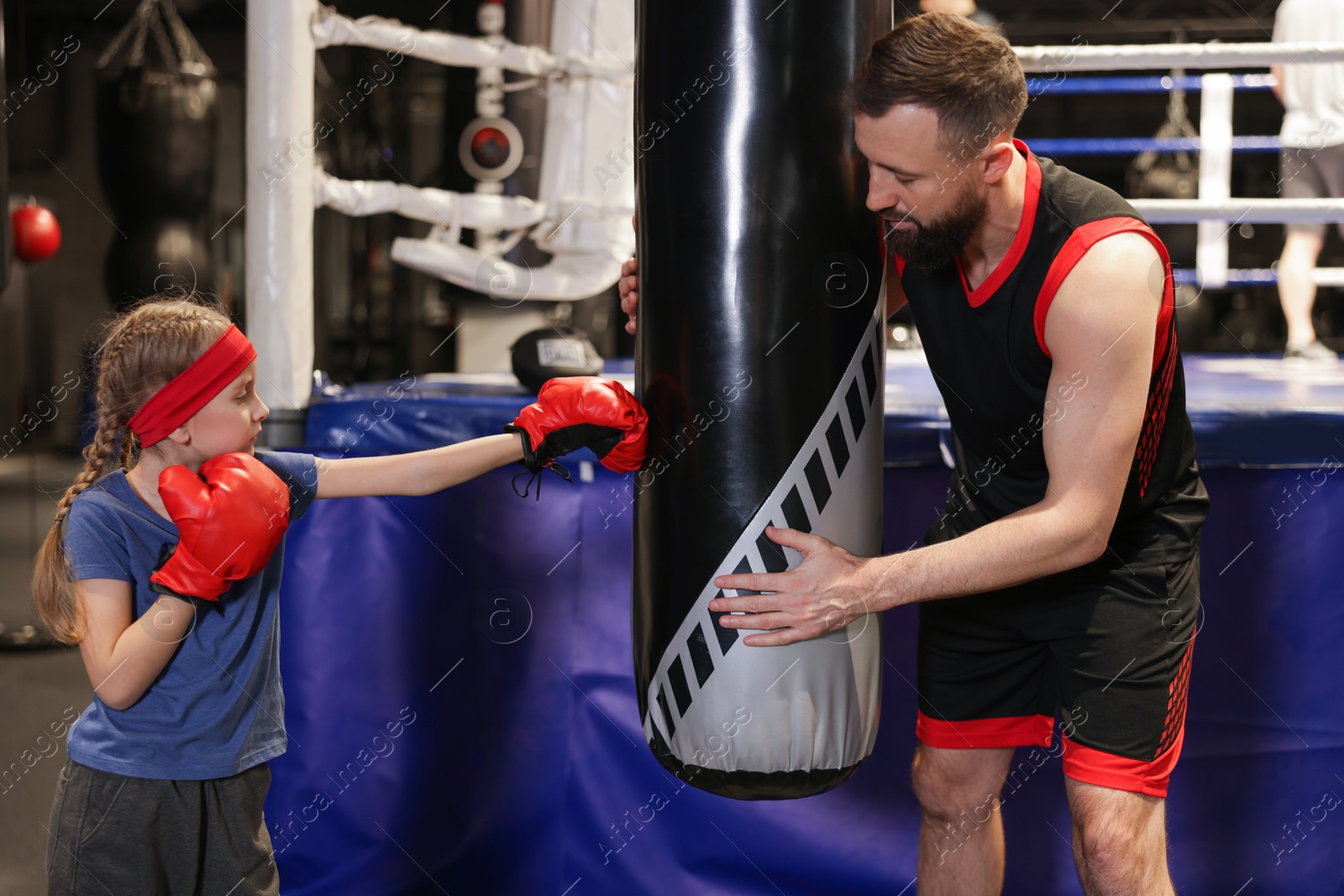 Photo of Girl in protective gloves having boxing practice with her coach at training center