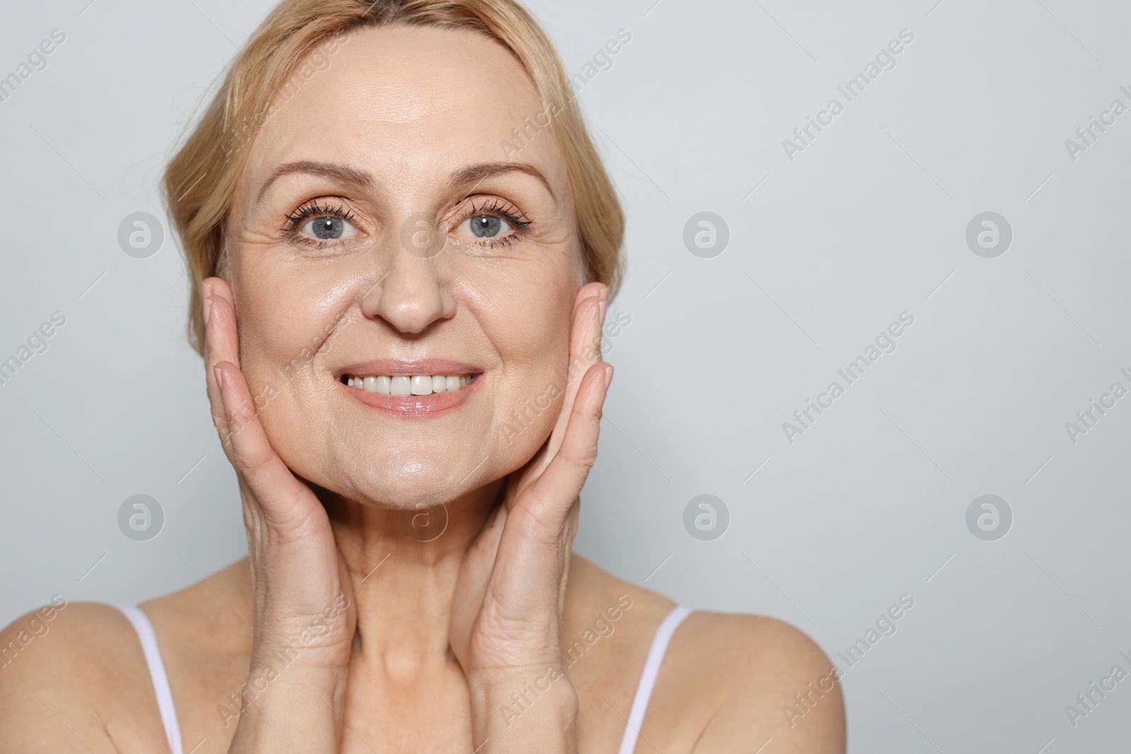 Photo of Portrait of smiling middle aged woman on grey background. Space for text