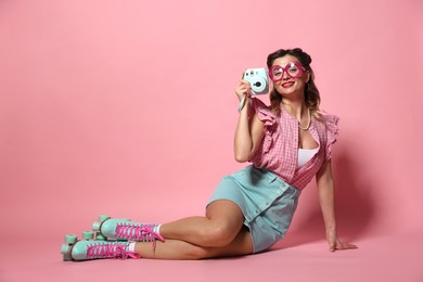 Happy pin-up woman wearing roller skates with camera on pink background, space for text