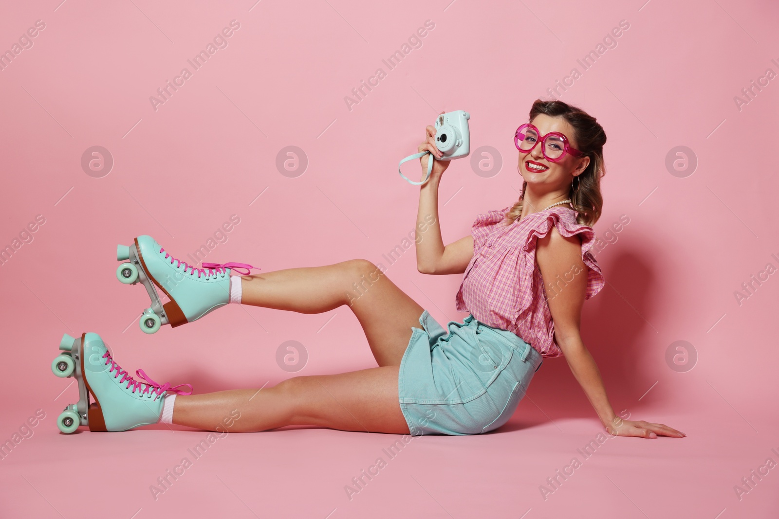 Photo of Happy pin-up woman wearing roller skates with camera on pink background