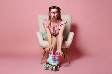 Photo of Attractive pin-up woman in roller skates sitting on armchair against pink background