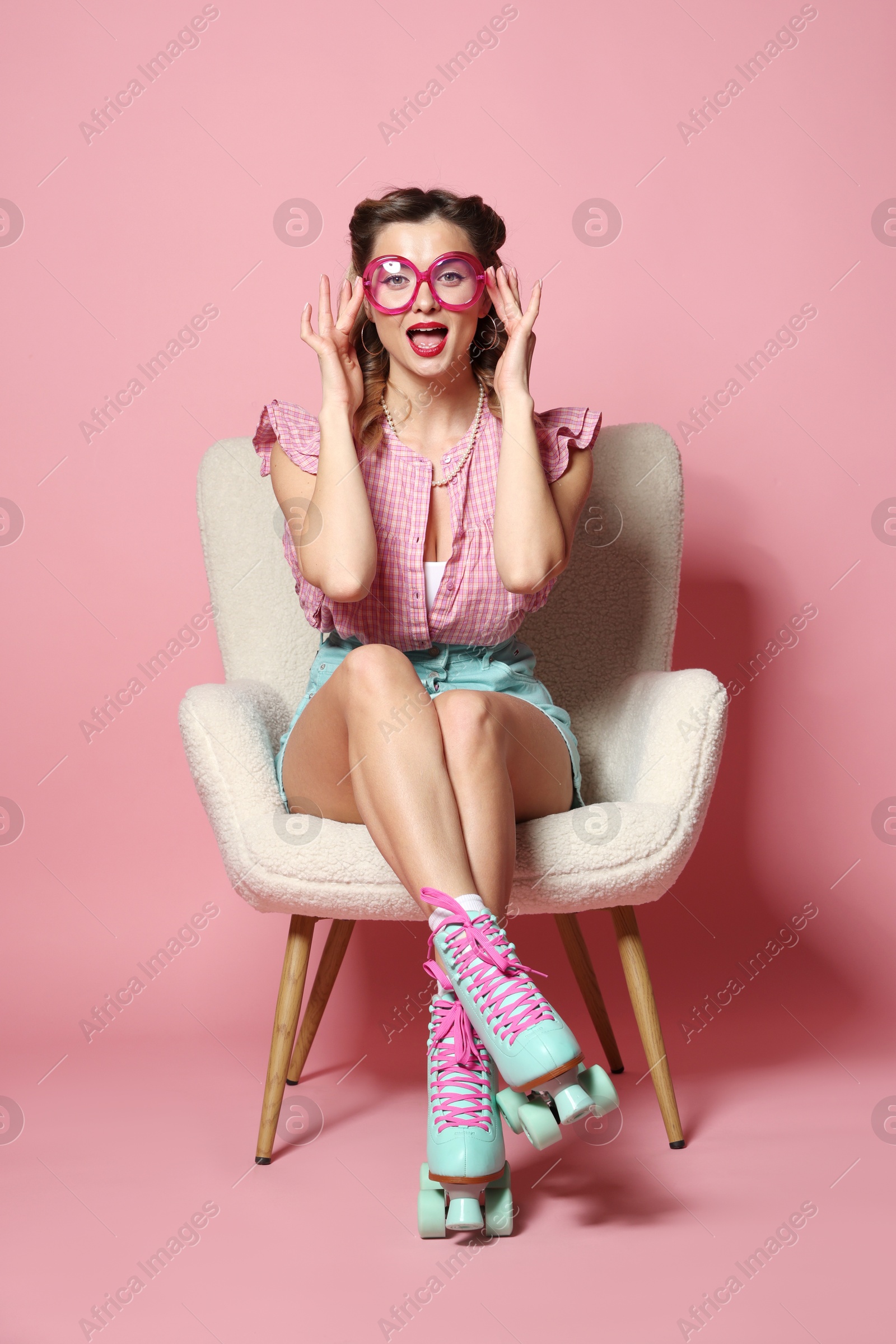 Photo of Attractive pin-up woman in roller skates sitting on armchair against pink background