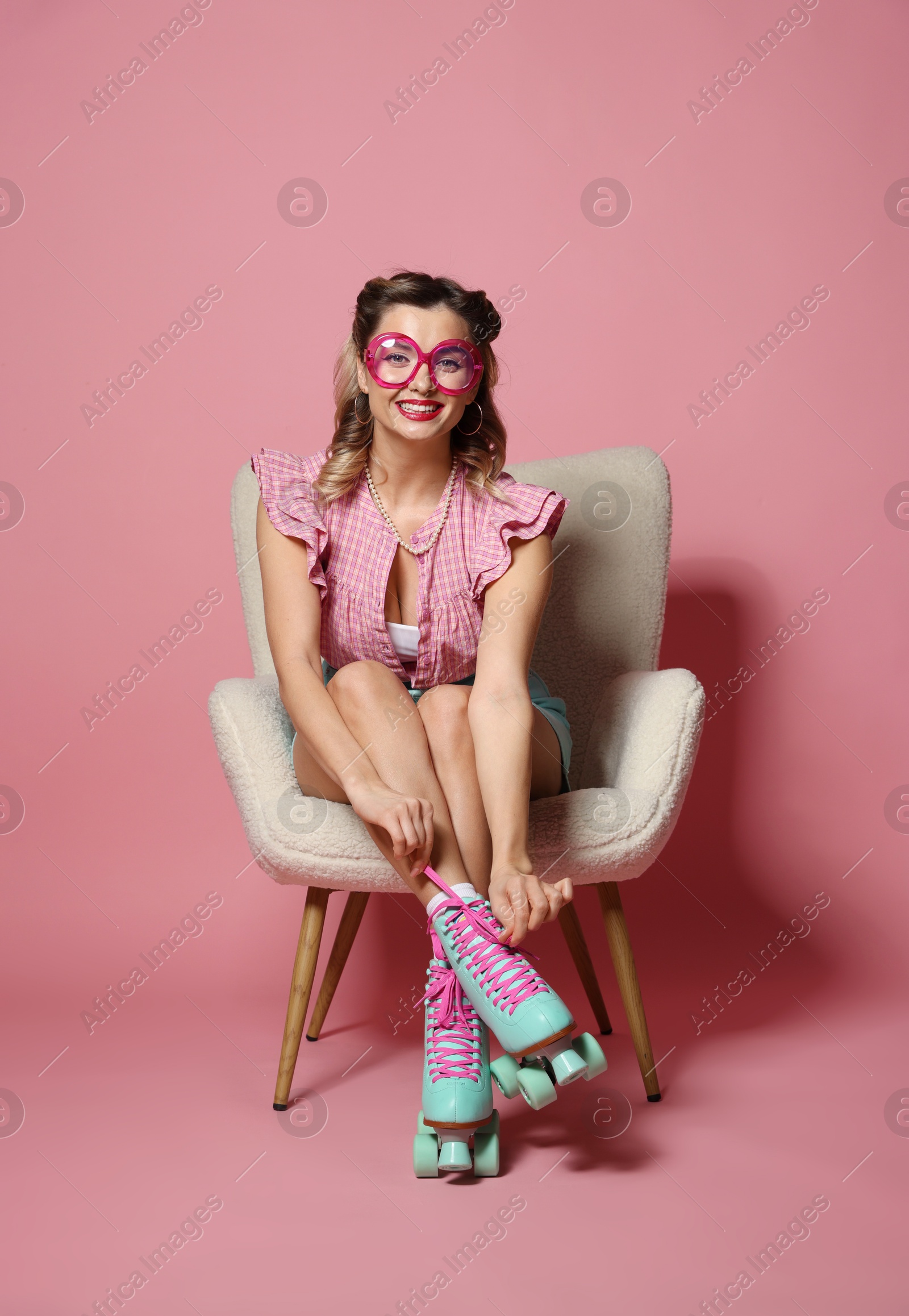 Photo of Happy pin-up woman in roller skates sitting on armchair against pink background