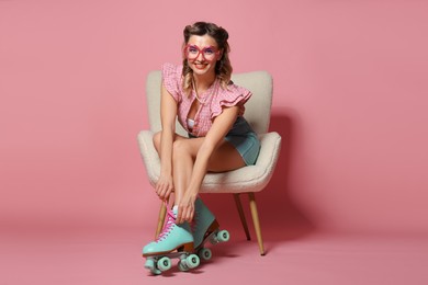 Happy pin-up woman in roller skates sitting on armchair against pink background