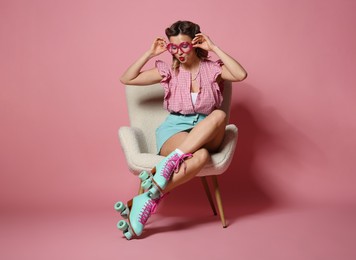 Photo of Attractive pin-up woman in roller skates sitting on armchair against pink background