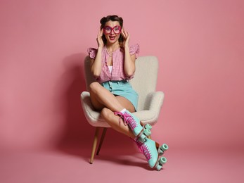 Photo of Happy pin-up woman in roller skates sitting on armchair against pink background