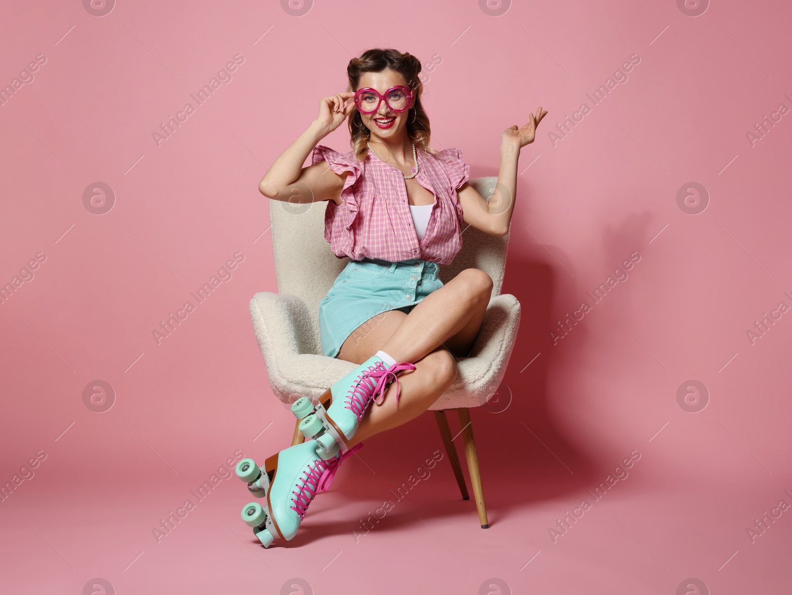 Photo of Happy pin-up woman in roller skates sitting on armchair against pink background