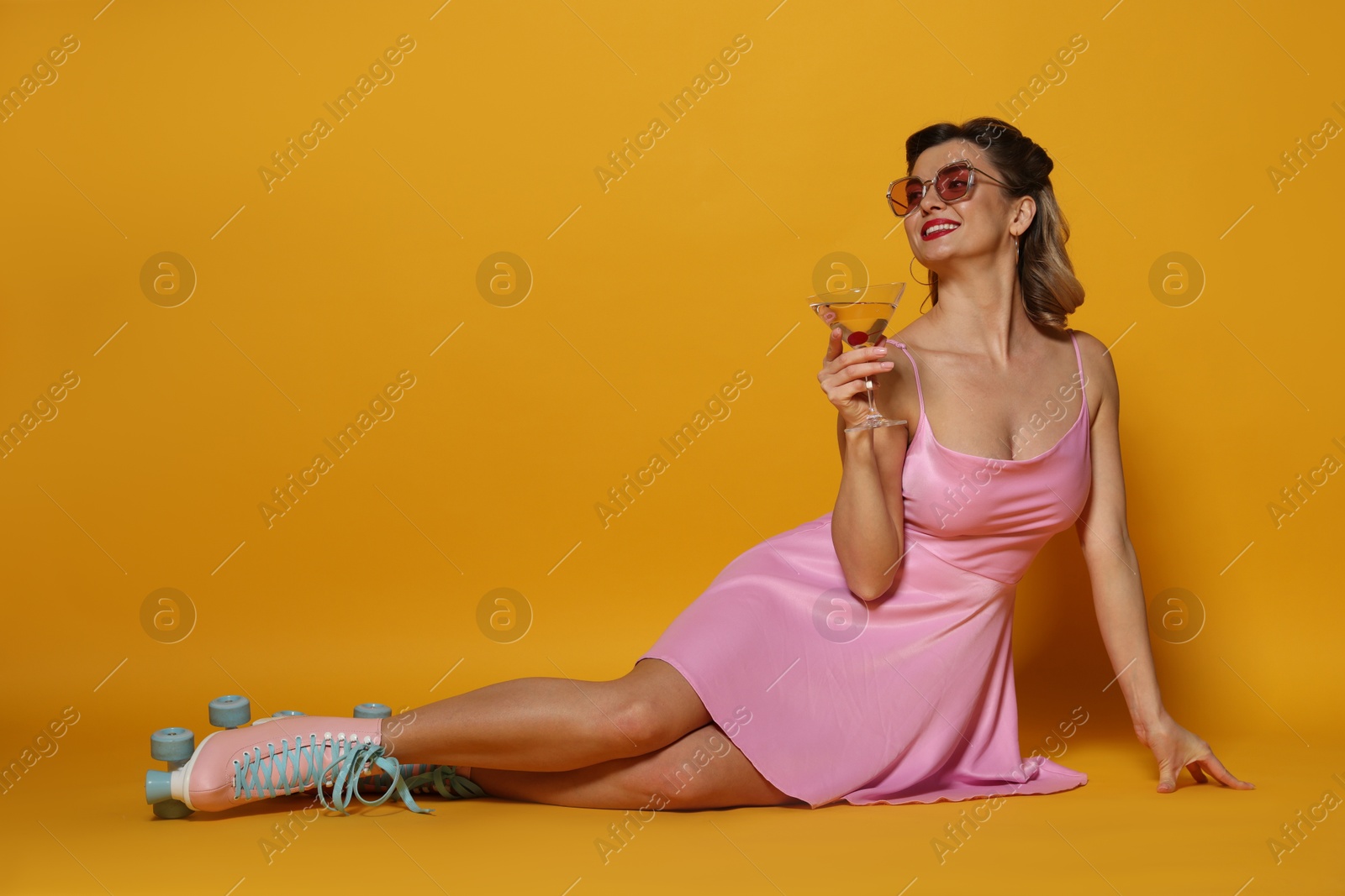 Photo of Happy woman in roller skates with cocktail posing on orange background, space for text. Pin-up vibes