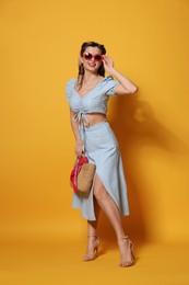 Photo of Happy pin-up woman in sunglasses posing with bag on orange background