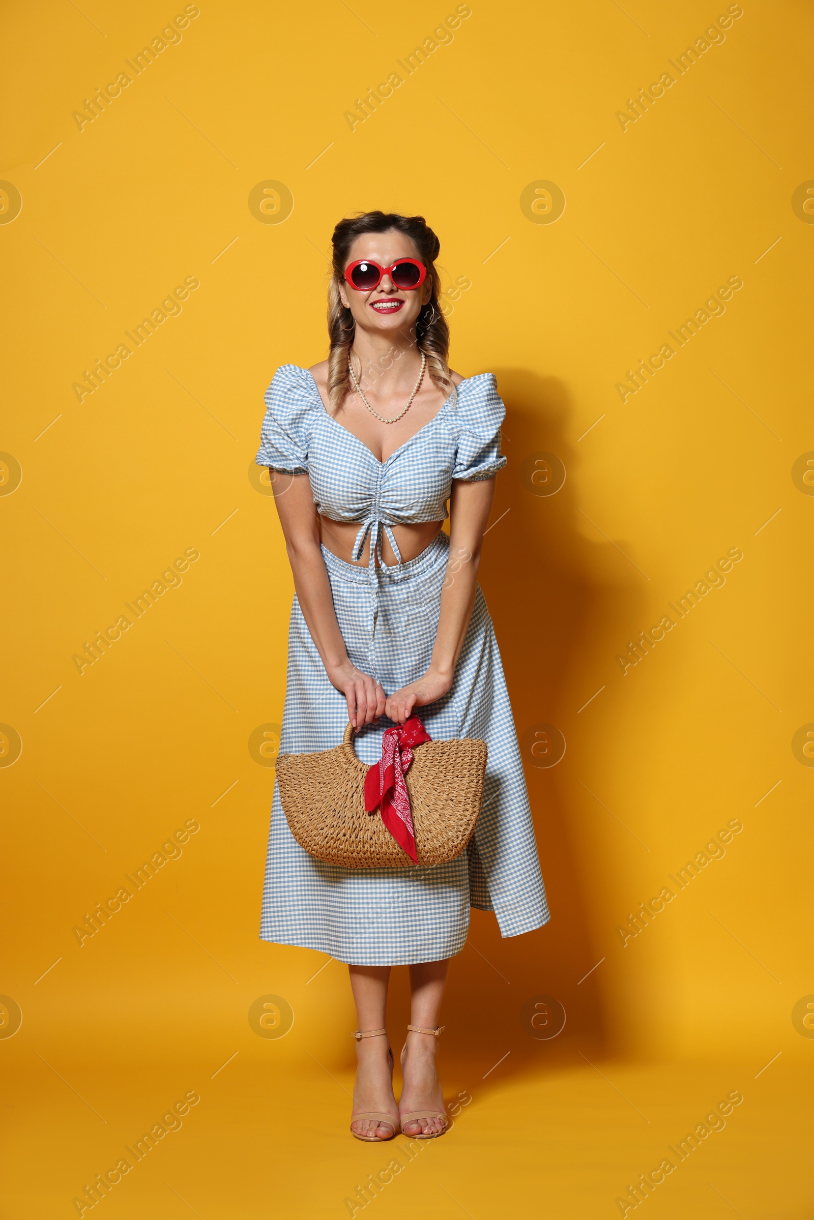 Photo of Happy pin-up woman in sunglasses posing with bag on orange background