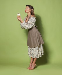 Photo of Beautiful woman with cupcake on green background. Pin-up vibes