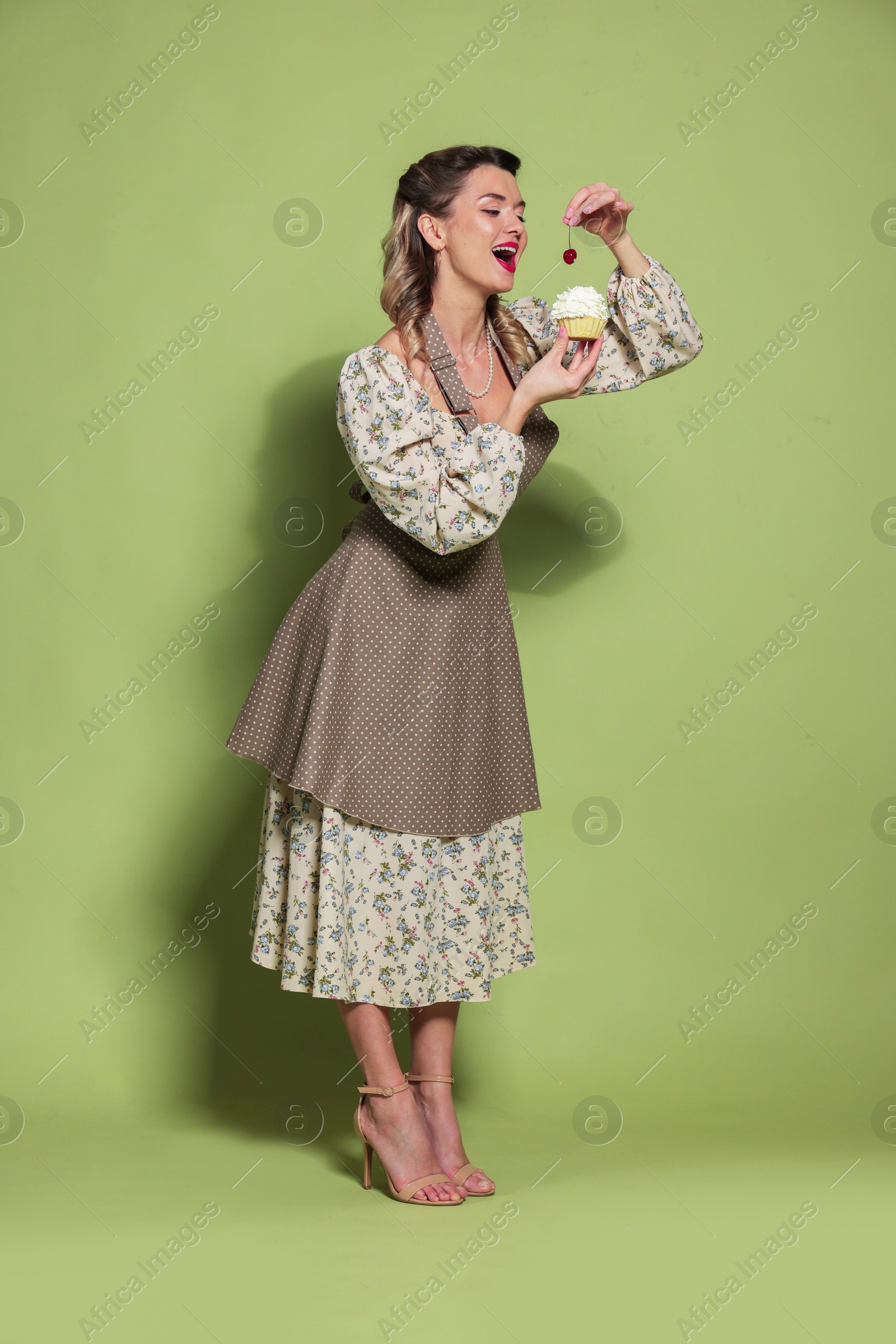 Photo of Beautiful woman with cupcake on green background. Pin-up vibes