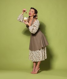 Photo of Beautiful woman with cupcake on green background. Pin-up vibes