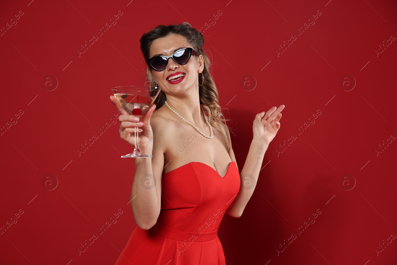 Photo of Happy woman with cocktail on red background. Pin-up vibe portrait