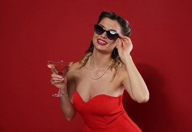 Photo of Happy woman with cocktail on red background. Pin-up vibe portrait