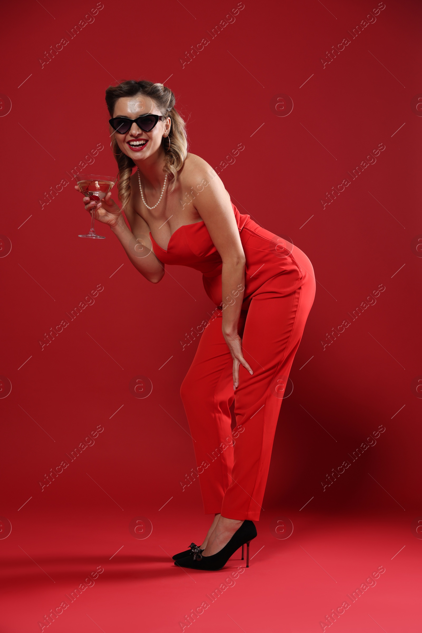 Photo of Happy woman with cocktail posing on red background. Pin-up vibes