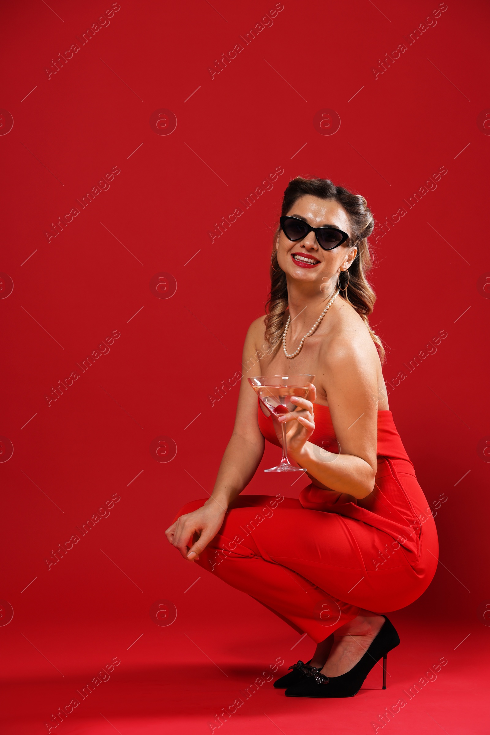 Photo of Happy woman with cocktail posing on red background. Pin-up vibes