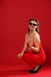 Photo of Happy woman with cocktail posing on red background. Pin-up vibes