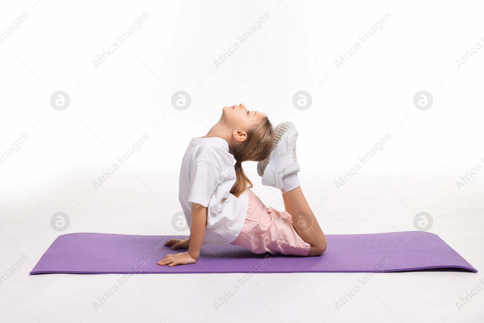 Photo of Little girl exercising on fitness mat against white background