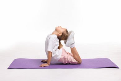 Photo of Little girl exercising on fitness mat against white background