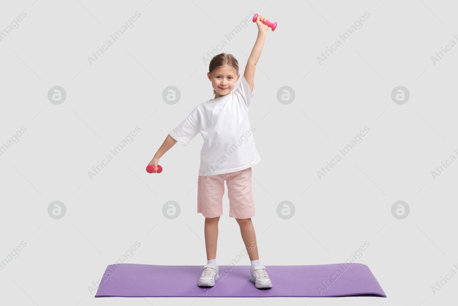 Photo of Little girl exercising with dumbbells on white background