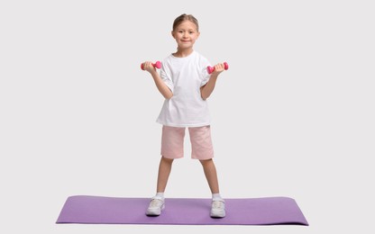 Little girl exercising with dumbbells on white background