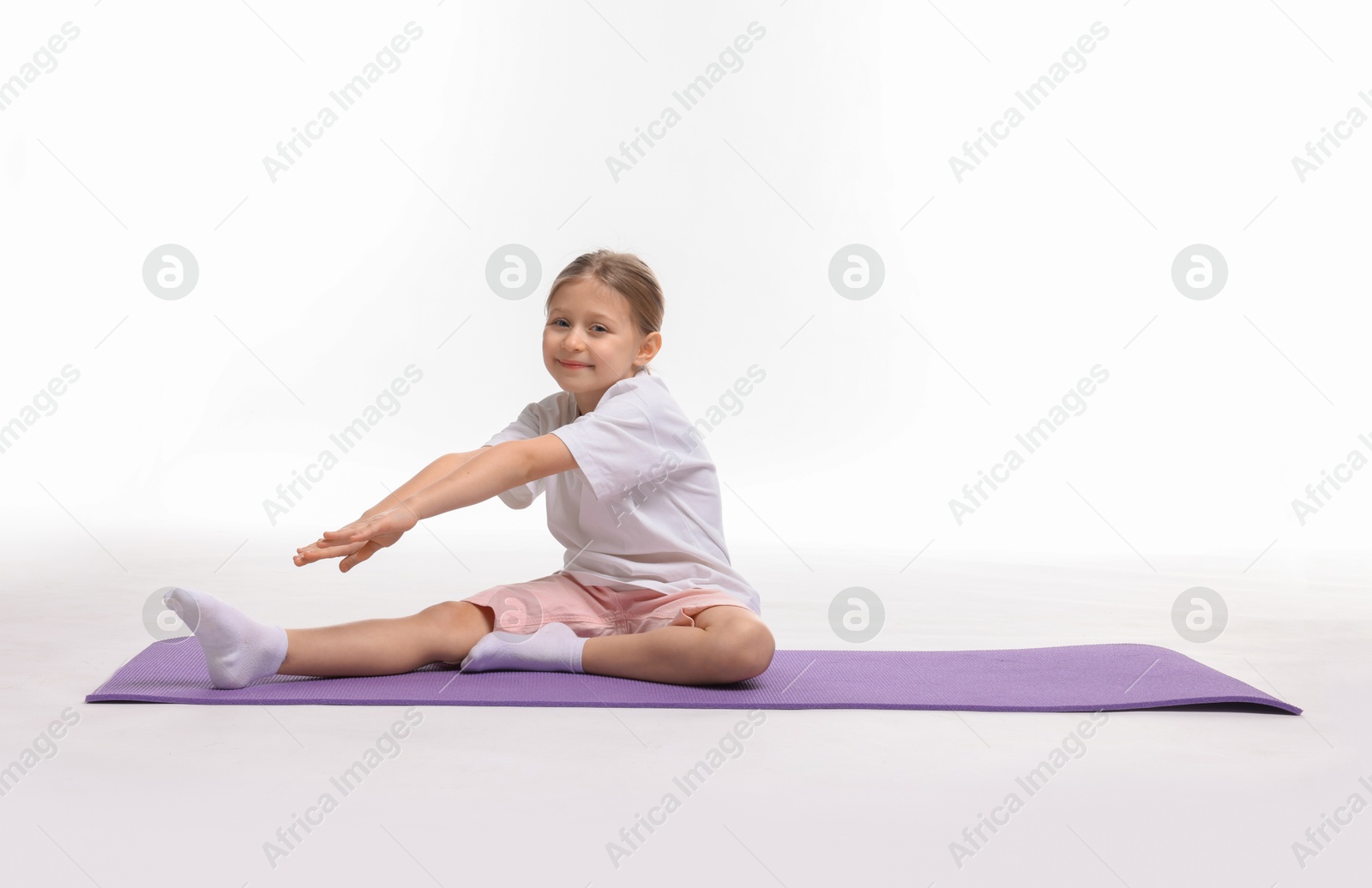 Photo of Little girl exercising on fitness mat against white background, space for text