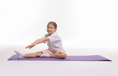 Little girl exercising on fitness mat against white background, space for text